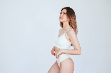 Beyaz kadın iç çamaşırları beyaz arka planda duruyor ve kollarını kaldırıyor. İdeal kadın vücudu. Boşluğu Kopyala.