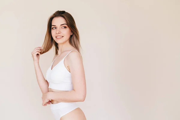 Young Woman White Underwear Stands Sideways Beige Background Cares Her — Stockfoto