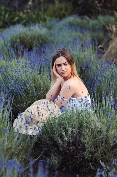 Young Gloomy Woman is frowning in Lavender Meadow. Portrait of girl sits upset in nature among lavender flowers