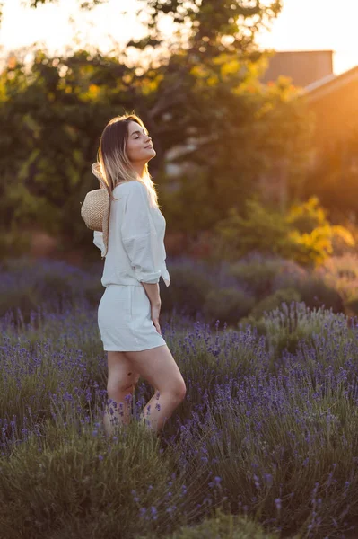 Romantic Woman in Lavender Fields Relaxing in Provence, France. Woman Walks through Lavender Fields at Sunset. Girl Stands in Lavender Fields with her Eyes Closed, Illuminated by Sunbeams of Sunset