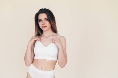 Bej Arkaplanda Beyaz Spor Top Stantları 'nda Sakin Genç Kadın. İç çamaşırlı kızın ideal figürü. Boşluğu Kopyala.