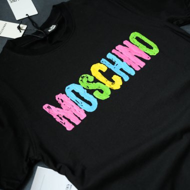 Nikopol, Ukrayna, Temmuz 1,2022: Moschino imzalı siyah tişört. Brand Giyim Düz Üst Görünümü. Tişörtte parlak parmak izi. Etiketli Yeni Giysilerle Alışveriş.