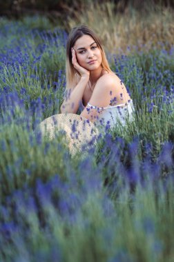 Vertical Photo Woman Sits among lavender, Looks thoughtfully into Camera. Girl without Retouching on Natural Background in lavender meadow outside city.
