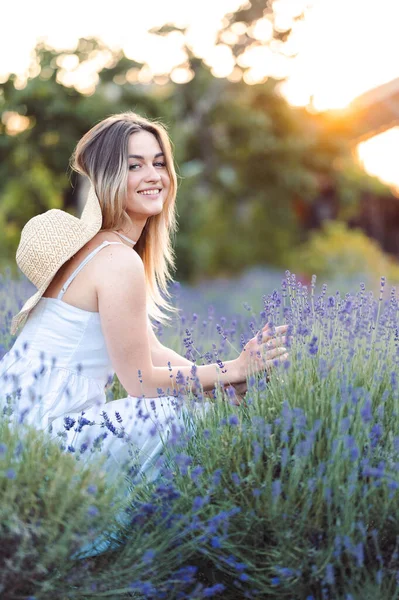 Vertical Portrait of Young Happy Woman in White Sundress Sitting Quietly Among Fresh Lavender. Stroke Lavender with Your Hand. Relax and Inhale Fresh Aroma of Lavender.