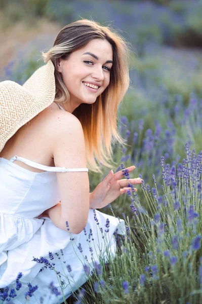 Vertical Portrait of Young Happy Woman in White Sundress Sitting among Fresh Lilac Lavender. Touch Hand to lavender. Relax and Inhale Fresh Aroma of Lavender.