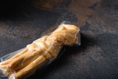 Smoked Cheese Pigtail Packed in Vacuum Bag. Grocery Goods on Dark Plane. Flat layout.