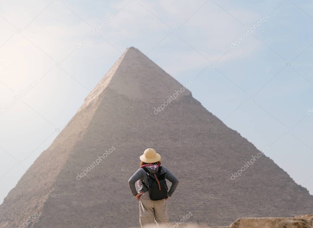 back view of tourist woman wearing a salacot standing on the sand in front of a pyramid. Egypt, Cairo - Giza