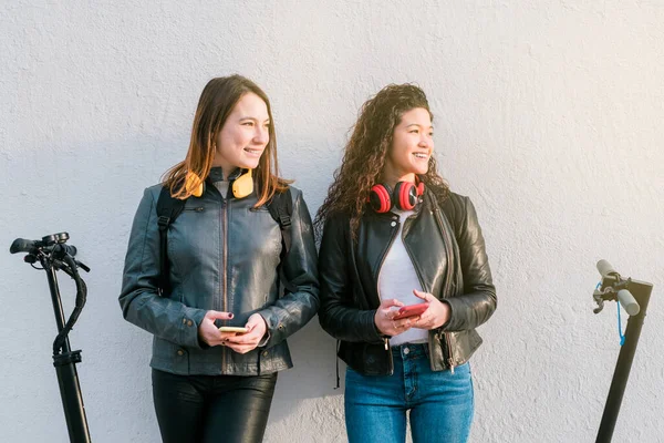屋外でスマートフォンを使用して電気スクーター上の2つの多民族女性の友人 高品質の写真 ストック写真