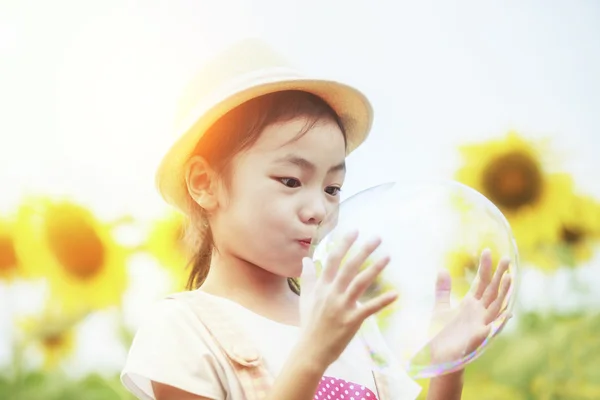 Asian little girl is blowing a soap bubbles in sunflower garden — Zdjęcie stockowe