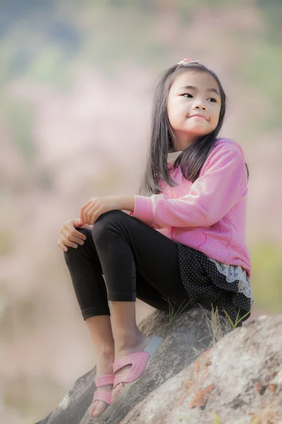 Маленькая азиатка сидит на скале с розовой сакурой — стоковое фото
