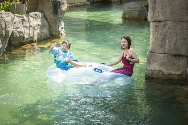 Asyalı çocukla annesi yazın yüzme havuzunda mayo giyip su parkında oynuyorlar.