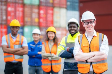 Konteynır deposunda yönetici ve ekip çalışması var. Lojistik ve ithalat merkezlerinde çalışan bir grup işçi ayakta duruyor ve gülümsüyor