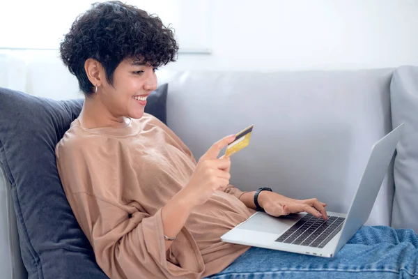 Latin woman shopping online by application in computer note book and pay monry online by credit card on sofa