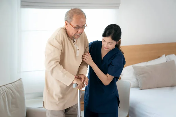 老人ホームでアジアの看護師は スタッフと一緒に立って歩くための老人をサポートします — ストック写真