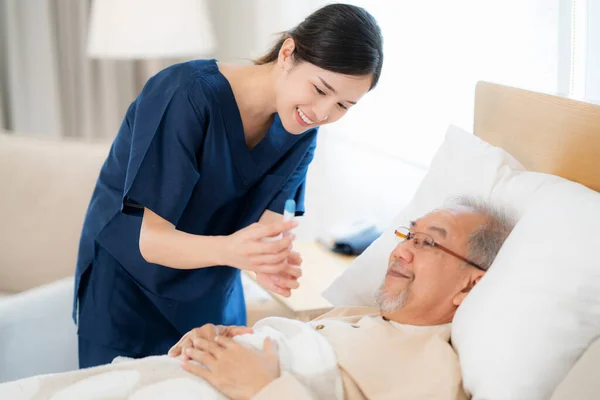 老人ホームでのアジアの看護師は 熱で体温をチェックするために老人をサポートします — ストック写真