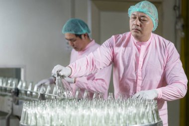 Fabrikadaki içki endüstrisinin üretim hattında aytomatik bir taşıyıcıda ham cam şişelerde çalışan Asyalı operatör.