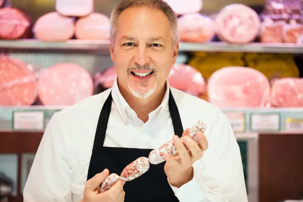 Mann zeigt Salami in einem Lebensmittelgeschäft — Stockfoto