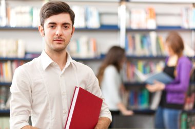 bir kitaplıkta duran erkek öğrenci