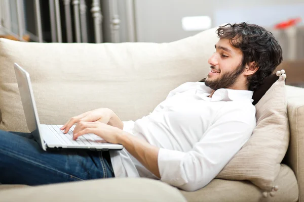 Ung man som kopplar av i soffan med en laptop — Stockfoto