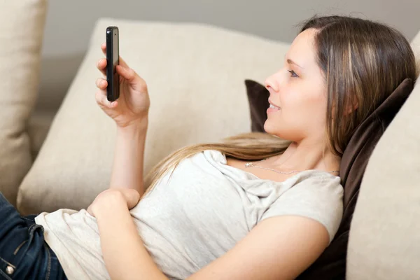 Schöne Frau entspannt sich auf dem Sofa mit ihrem Smartphone — Stockfoto