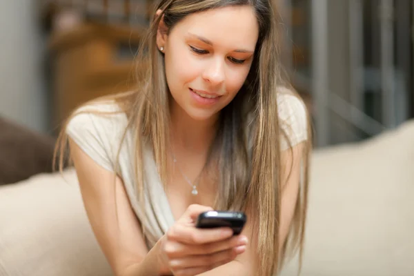 Schöne Frau sitzt mit ihrem Smartphone auf dem Sofa — Stockfoto