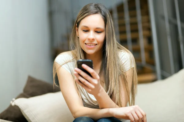 Vacker kvinna sitter i soffan med sin smartphone — Stockfoto