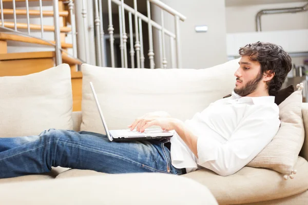 Jovem relaxante no sofá com um laptop — Fotografia de Stock