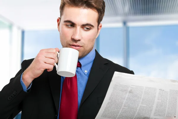 Empresario leyendo un periódico mientras bebe café — Foto de Stock