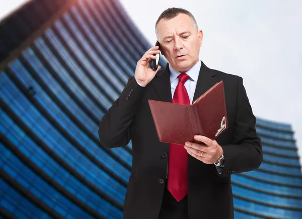 Reifer Geschäftsmann macht sich in seinem Büro Notizen am Telefon — Stockfoto