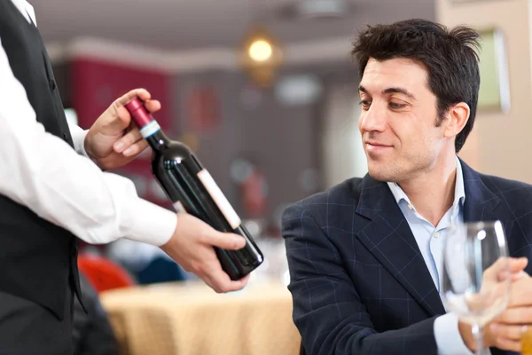 Waiter suggesting a bottle of wine to a customer Stock Picture