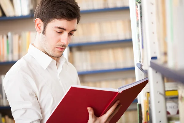 Un tizio che legge un libro in una biblioteca — Foto Stock