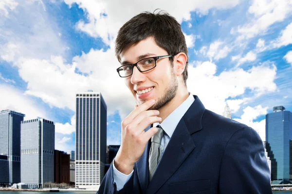 Lächelnder junger Geschäftsmann vor Wolkenkratzern — Stockfoto