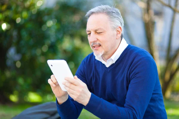 Äldre man med hjälp av en digital tablet i parken — Stockfoto