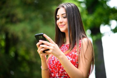 Parkta, dışarıda akıllı telefonunu kullanan genç ve güzel bir kadın.