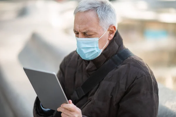 Covidコロナウイルスのライフスタイル マスクされた高齢者ビジネスマン彼のタブレットを使用して市の広場に屋外に座っている間 — ストック写真