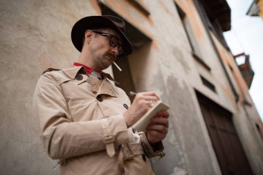 Dedektif eski bir duvara karşı dururken bir not defterine yazma