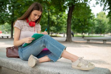 Okulun önündeki parkta ders çalışan bir kız öğrencinin portresi.
