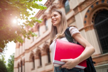 Okulunun önünde kitap tutan genç bir kız öğrenci.