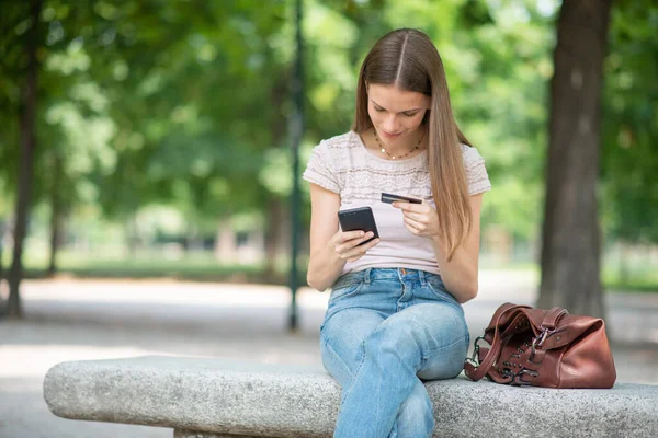 妇女坐在公园外 用信用卡在网上购物 — 图库照片