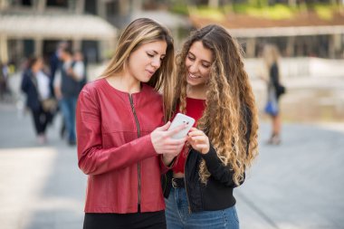 Şehirde cep telefonu kullanan gülümseyen kadınlar.
