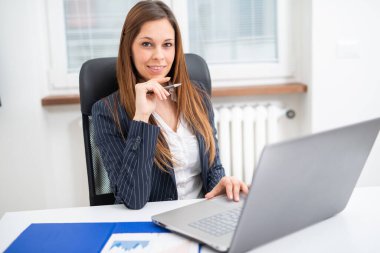 Ofisinde dizüstü bilgisayar kullanan gülümseyen bir kadın.