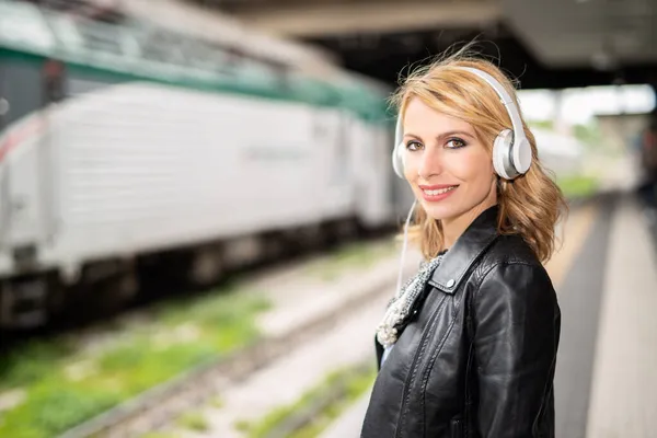 年轻女人在等火车听音乐 — 图库照片