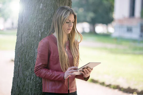 Genç Bir Kadın Parkta Bir Ağaca Yaslanırken Dijital Tablet Kullanıyor — Stok fotoğraf