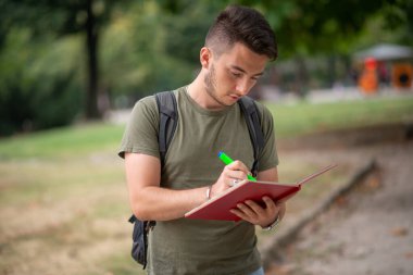 Erkek öğrenci parkta notlar yazıyor.