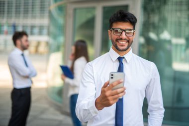 Bir grup iş arkadaşının önünde cep telefonunu kullanarak gülümseyen işadamı, takım çalışması kavramı