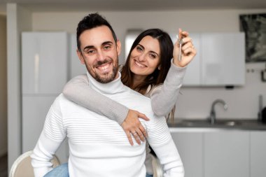 Mutlu çift yeni evlerinde sarılıyor, kadın yeni anahtarları gösteriyor.