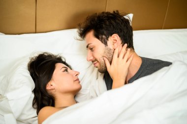 Genç çift battaniyenin altında sarılıyor.