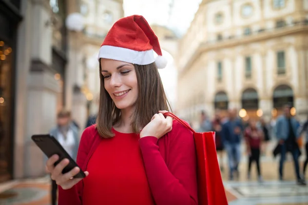 Usmívající Mladá Žena Nakupování Při Rozhovoru Telefonu Sobě Vánoční Klobouk — Stock fotografie