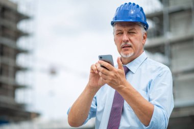 Düşünceli mimar gözlerini kapatıyor ve akıllı telefonunu kullanarak düşünüyor.