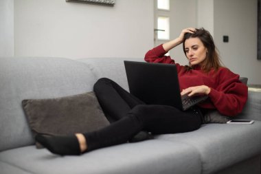 Genç bir kadın evinde dinlenirken dizüstü bilgisayar kullanıyor.